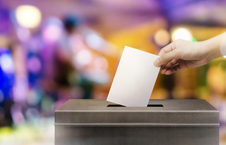 A person's hand dropping a vote in a ballot box on election day