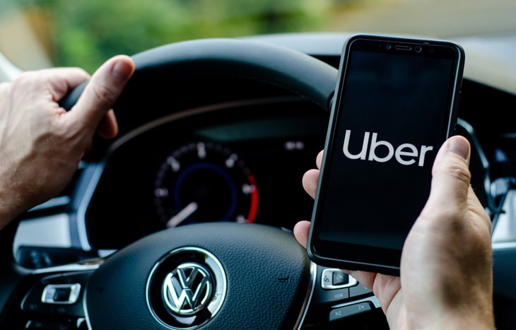 An Uber driver holding his phone while steering his car and using the Uber app.