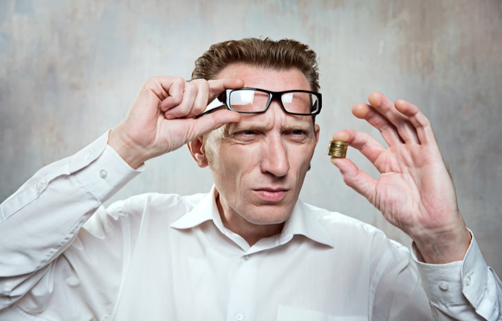 A man lifts his spectacles up to examine a tiny bit of money in his hands. Here's how to invest in the stock market for beginners with little money.