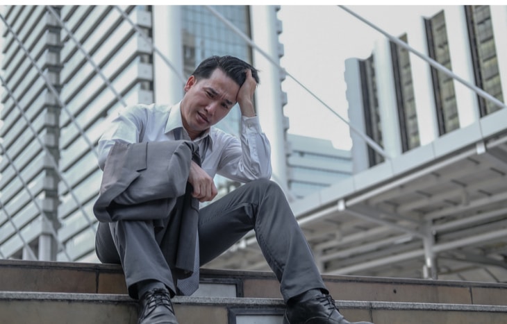 A stock trader sitting on some stone steps looking sad. How bad will the 2020 recession be?