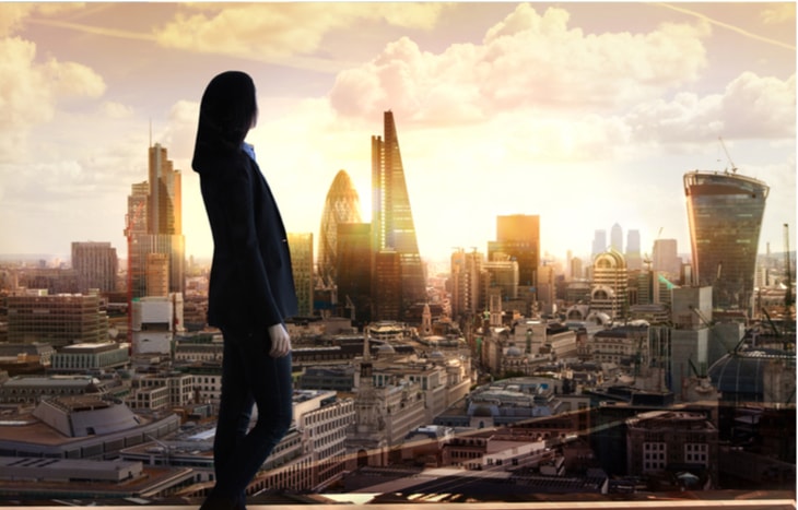 A business woman looking out over a city skyline at investment opportunities during a stock market correction at sunset | Investment U