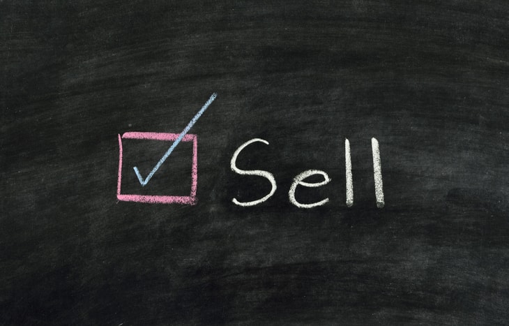 The word “sell” on a blackboard next to a marked checkbox. We’ll explain to you when to sell stocks as an investor.