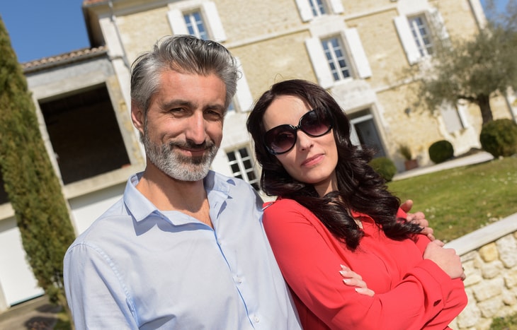 A happy couple in front of their home who are building wealth in their 40s.