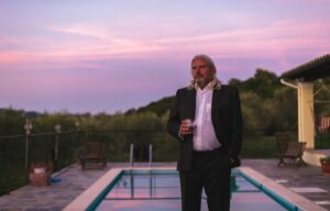 A middle-aged man by his swimming pool at dusk as he's building wealth in his 50s.