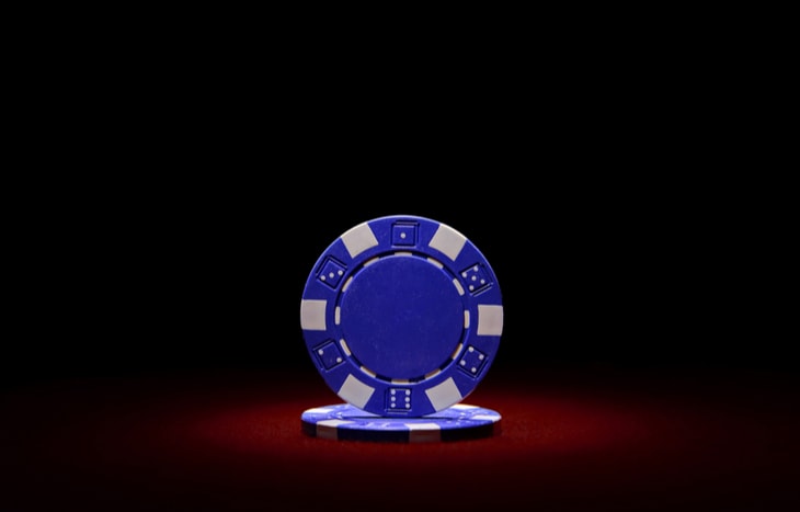 A blue poker chip against a dark red and black background representing the disadvantages of blue chip stocks.